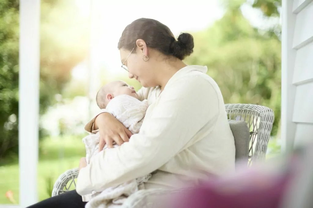 A mother sitting on a beautiful deck holding her tiny baby close to her chest